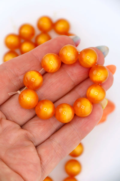 Hand holding a strand of 12mm Orange Moon Glow Italian Poly Resin Round, 10 Beads