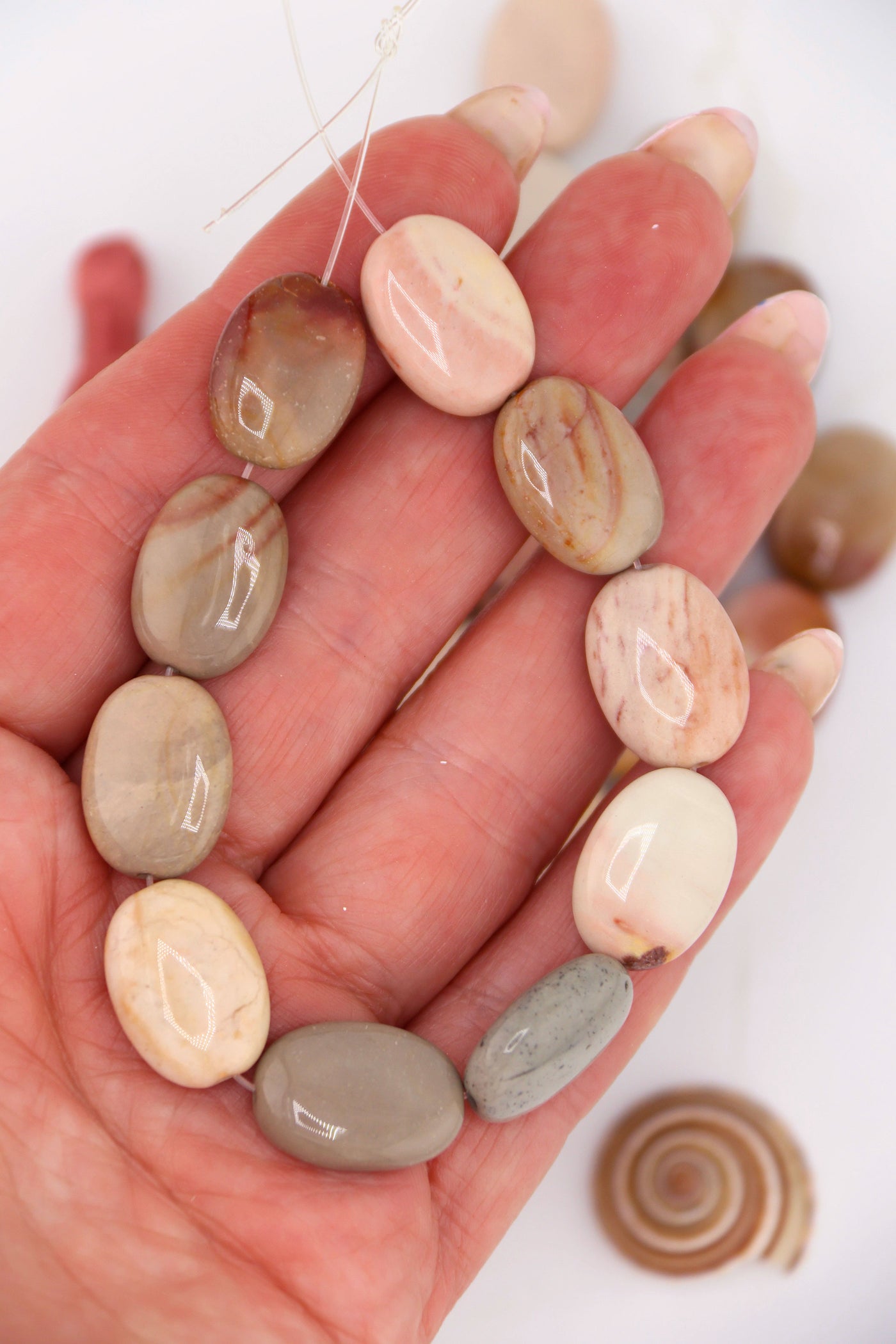 Hand holding strand of Imperial Jasper oval beads, 13x18mm, polished gemstones in earthy neutral and pastel tones.