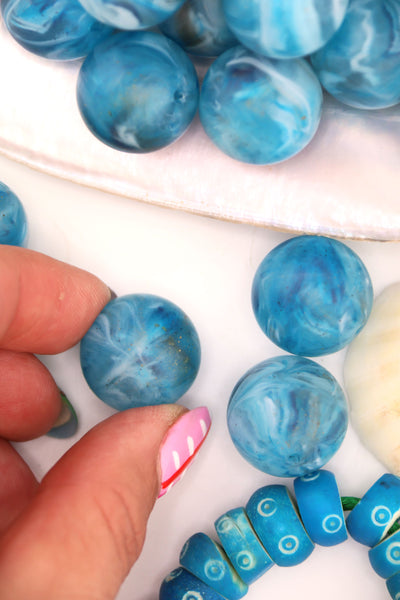Turquoise blue swirly beads that look like earth, with fingers holding one of the beads.