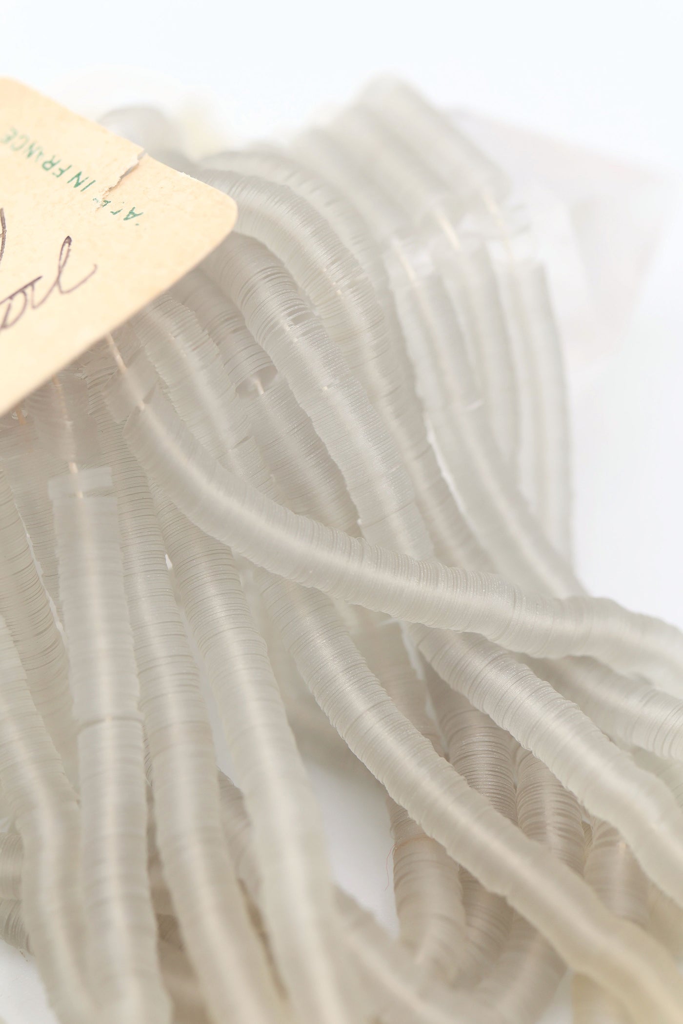 Hank of clear grey vintage French sequins draped so their iridescent faces are showing, and the vintage tag with handwriting.