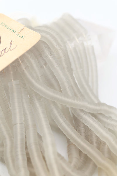 Hank of clear grey vintage French sequins draped so their iridescent faces are showing, and the vintage tag with handwriting.