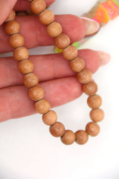 Hand holding a strand of 8mm round wood beads in natural finish, lightweight beads made in India