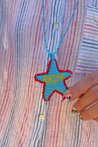 Model wearing a hand-beaded star pendant necklace handcrafted by Colombian artisan moms in bright primary colors.
