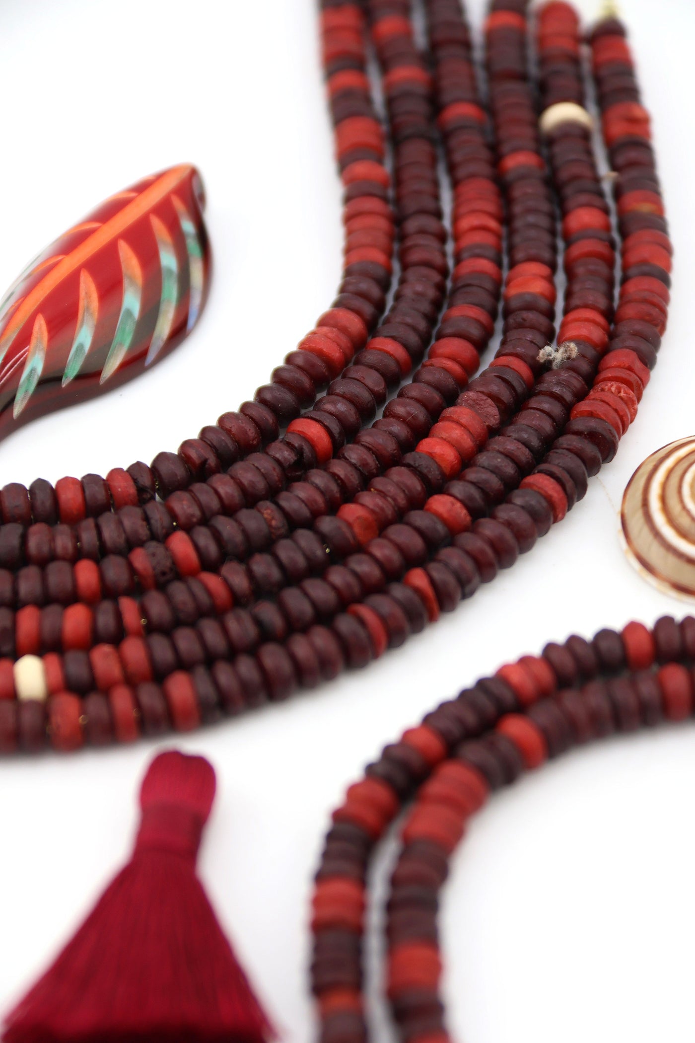 Flatlay of burgundy and rustic red bone heishi beads in strands, handmade and ethically sourced, styled with tassel and decorative accents.
