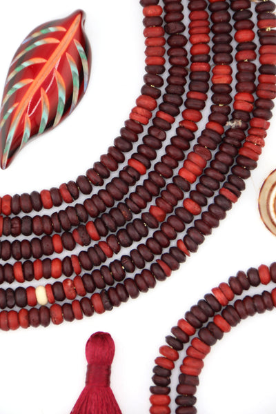 Strands of deep burgundy and red bone heishi beads arranged on white background with bohemian acc