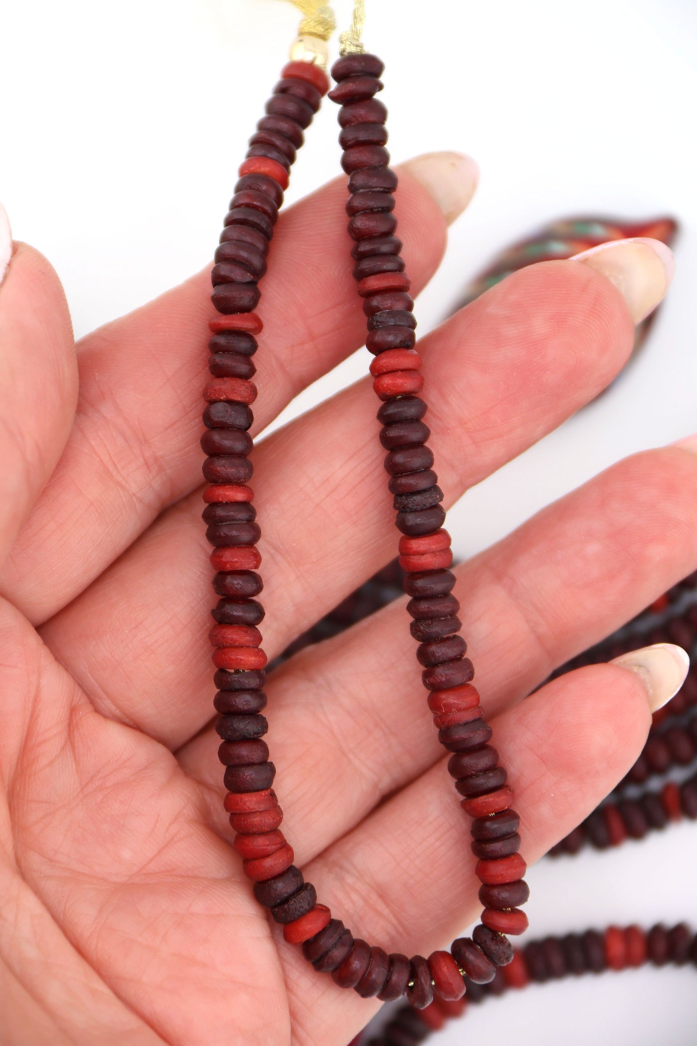 Hand holding strand of burgundy bone heishi beads, 6x3mm size, handmade from ethically sourced bone
