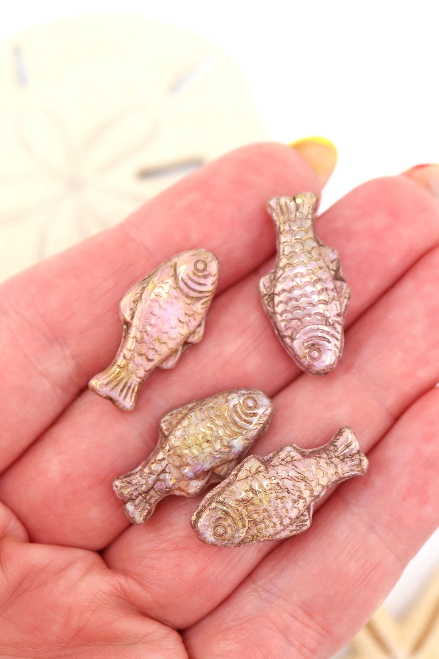 Hand holding four mauve and pink Czech glass fish beads with golden wash and vintage-inspired finish.

