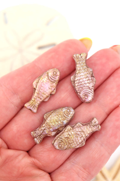 Hand holding four mauve and pink Czech glass fish beads with golden wash and vintage-inspired finish.

