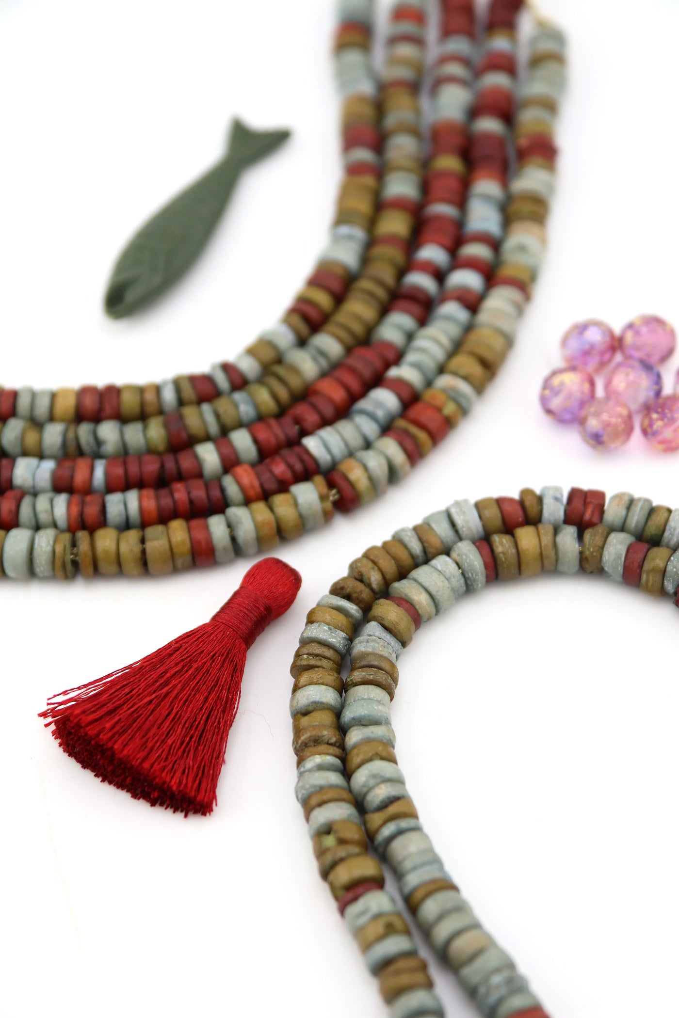 Ethically sourced bone heishi beads in warm neutral tones, 8x3mm, styled with red tassel and fish charm accent.