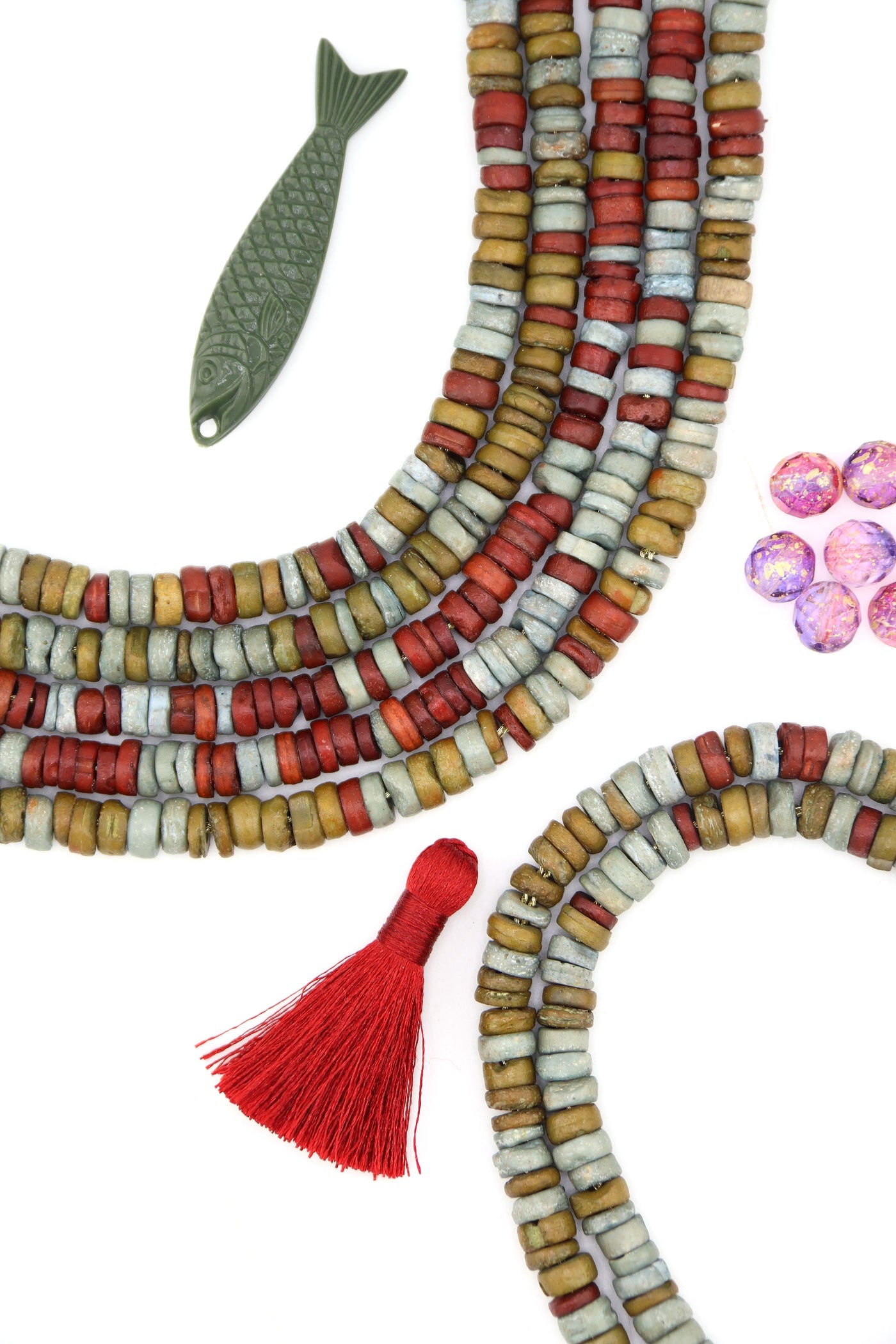 Handmade bone beads in earthy sage, clay red, and ochre arranged in layered strands on a white background.