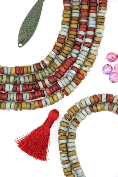Handmade bone beads in earthy sage, clay red, and ochre arranged in layered strands on a white background.