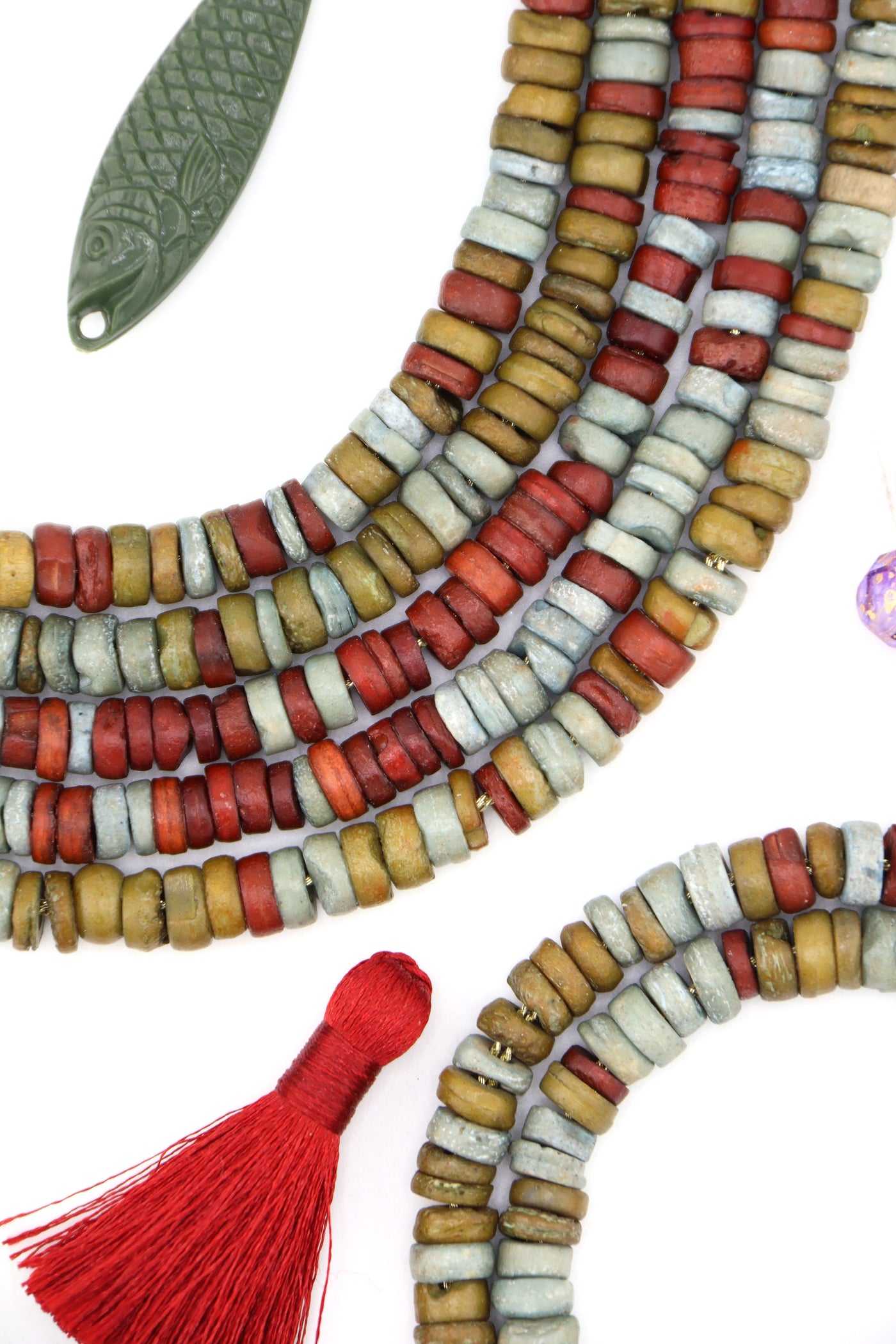Close-up of rustic bone heishi beads in earthy neutral colors, including green, red, and ochre, arranged in strands.