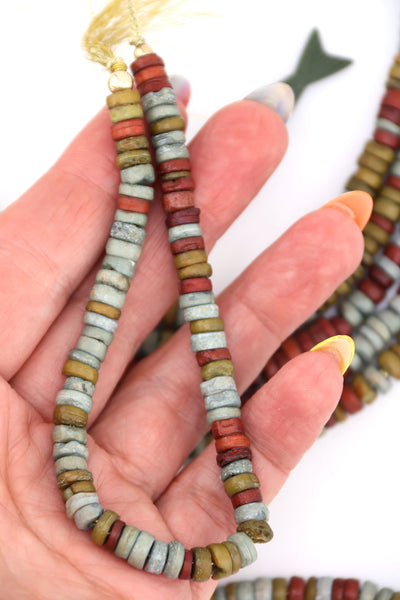 Handmade bone beads in earthy sage, clay red, and ochre arranged in an outstretched palm.