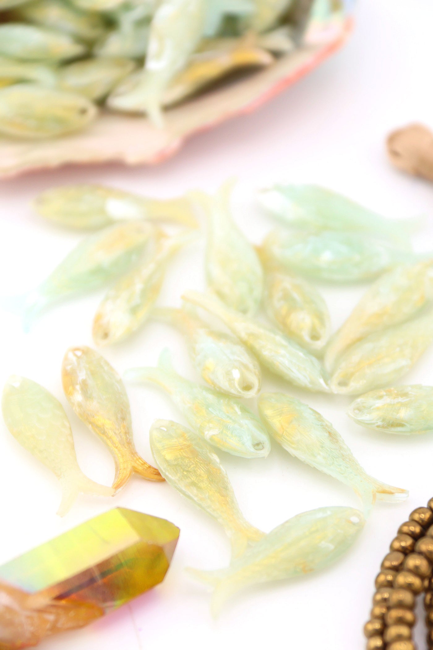 Flatlay of German resin fish charms in soft green with gold accents, perfect for DIY jewelry and crafts.