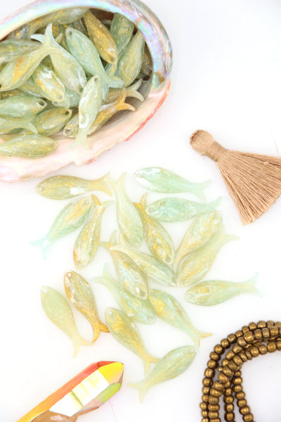 Close-up of handmade Golden Sage resin fish beads with carved scale pattern, shimmering in the light.