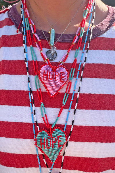 Person wearing stacked beaded HOPE heart necklaces layered over a red and white striped shirt.