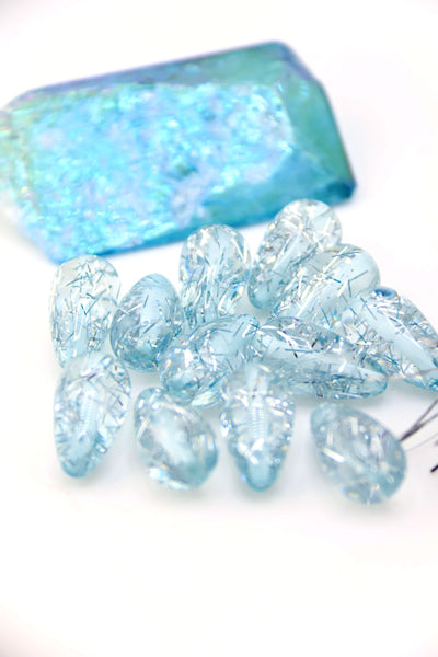 Collection of Ice Blue Glitter Italian Resin Teardrop Beads on a white background with a blue crystal