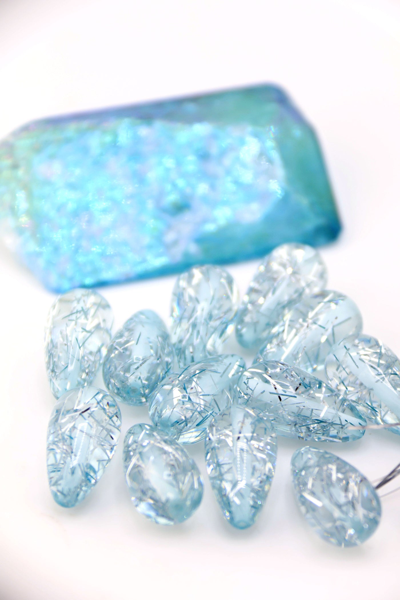 Collection of Ice Blue Glitter Italian Resin Teardrop Beads on a white background with a blue crystal