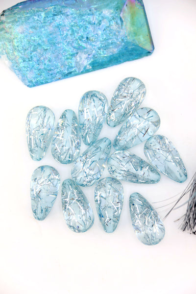 Collection of Ice Blue Glitter Italian Resin Teardrop Beads on a white background with a blue crystal