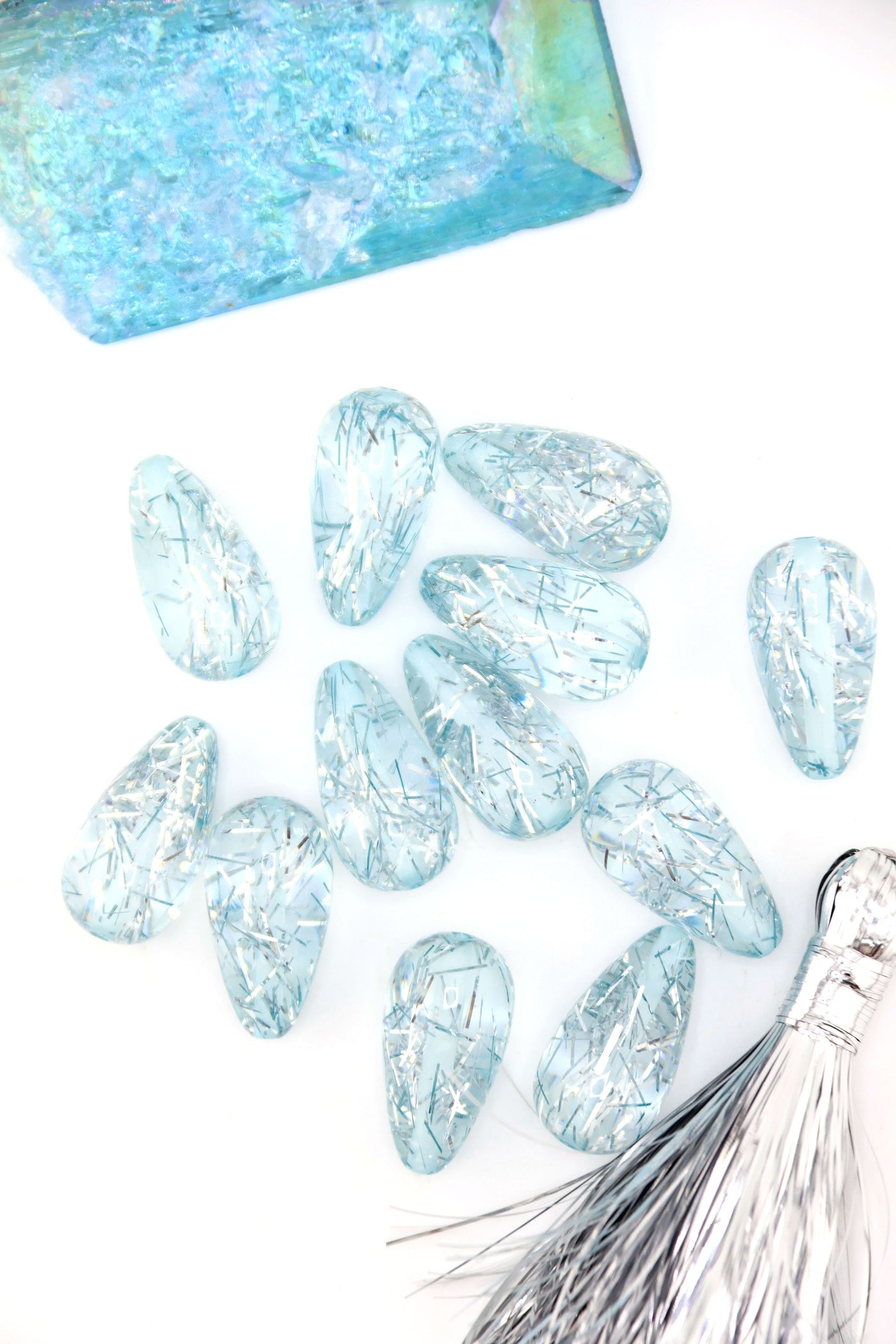 Collection of Ice Blue Glitter Italian Resin Teardrop Beads on a white background with a blue crystal