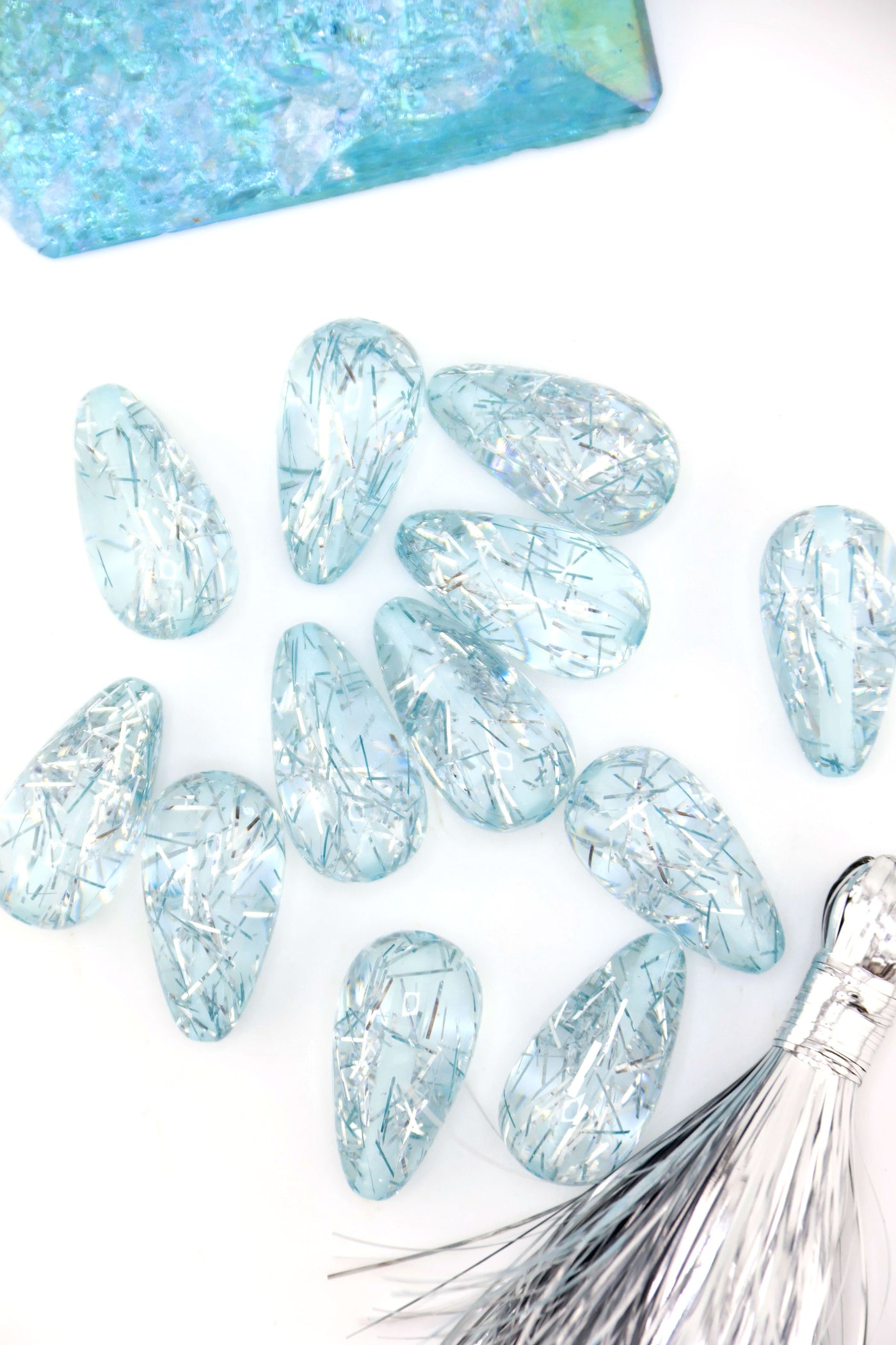 Collection of Ice Blue Glitter Italian Resin Teardrop Beads on a white background with a blue crystal