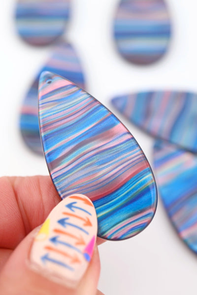 Fingertips with arrow manicure, holding a Blue Galaxy Waves Teardrop Laser Cut Italian Poly Resin Pendant 