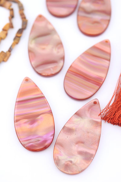 Close-up of warm iridescent Italian polyresin teardrop pendants in copper, rose gold, and pink tones, displayed on a white background.