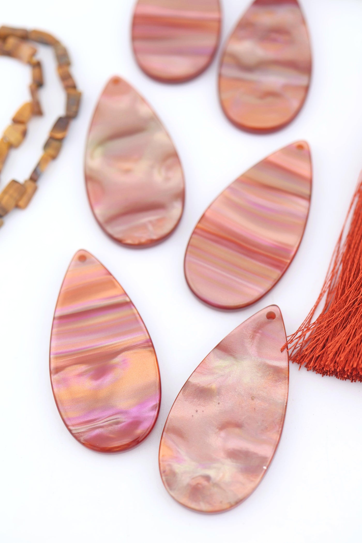 Close-up of warm iridescent Italian polyresin teardrop pendants in copper, rose gold, and pink tones, displayed on a white background.