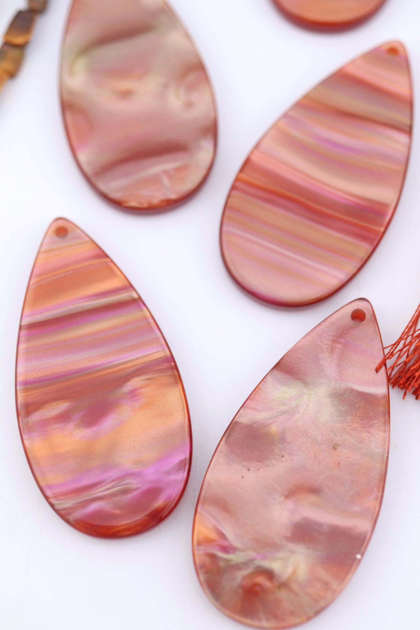 Close-up of warm iridescent Italian polyresin teardrop pendants in copper, rose gold, and pink tones, displayed on a white background.
