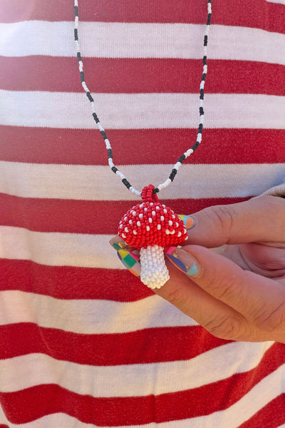 Hand holding a hand-beaded red and white dotted mushroom charm, on a black and white seed bead necklace.