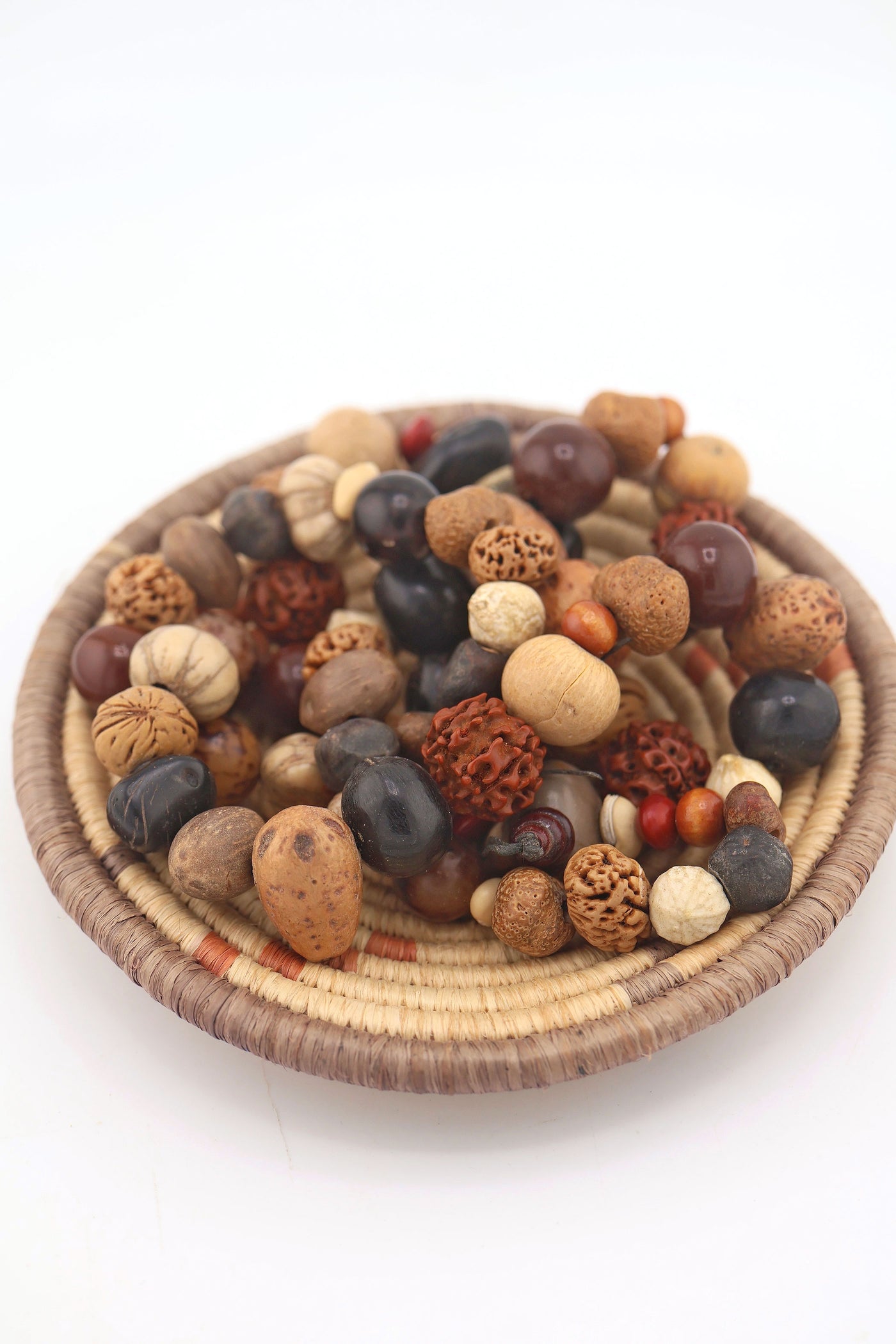 Strand of assorted natural nut and seed beads in earthy brown, tan, and black tones, featuring rudraksha and palm nuts, in a woven basket.