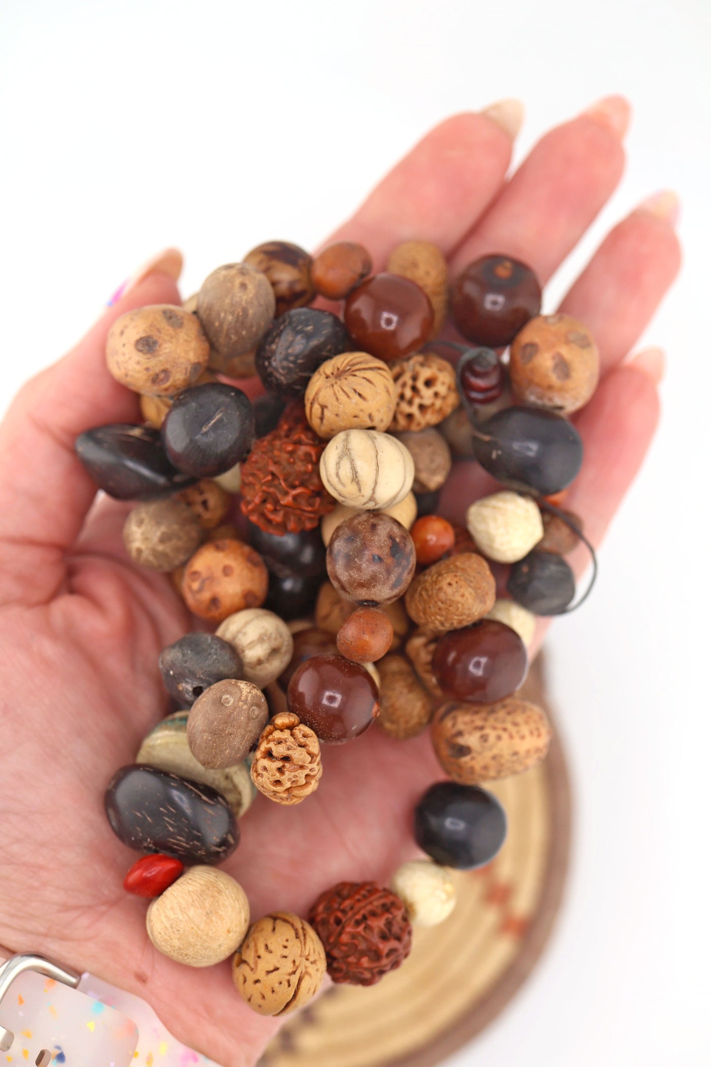 Strand of assorted natural nut and seed beads in earthy brown, tan, featuring rudraksha and palm nuts, in a hand.