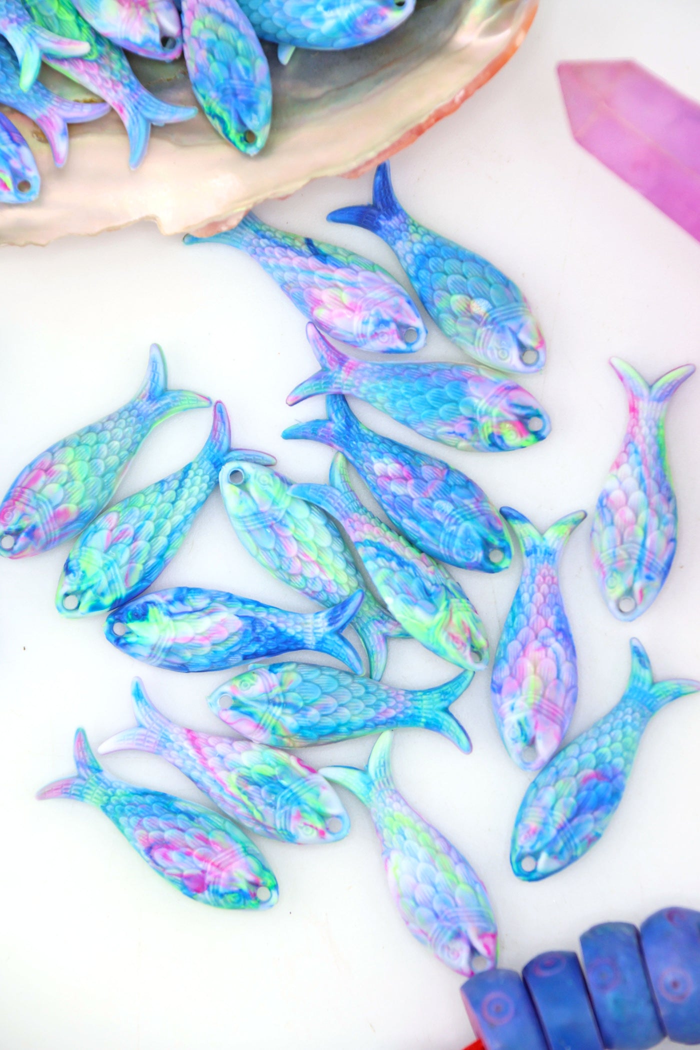 Pastel Aurora resin fish charms in swirls of blue, pink, lavender, and green, styled on white background with shell.