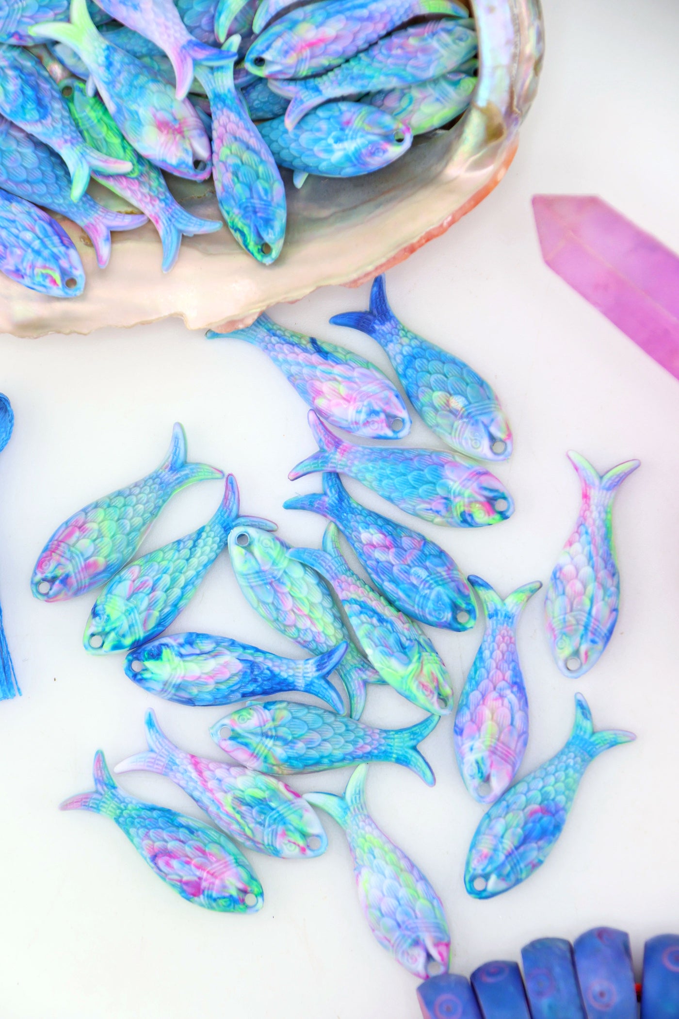 Colorful resin fish charms in pastel aurora tones of blue, pink, and green, arranged with a seashell.