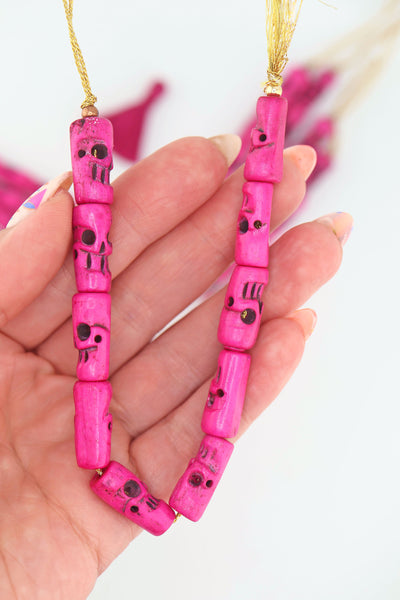 Strand of pink hand-carved skull beads in the palm of a hand.