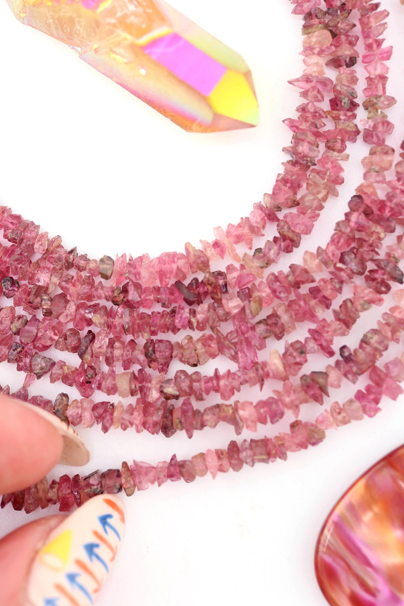Hand adjusting a strand of pink tourmaline beads, showing color variations from pale pink to deep magenta.