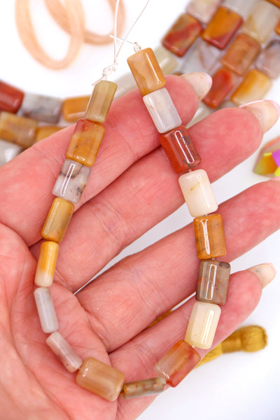 Hand holding strand of genuine Sansha Jasper puffed rectangle beads in earthy gold, cream, terracotta, and gray tones, polished and glossy