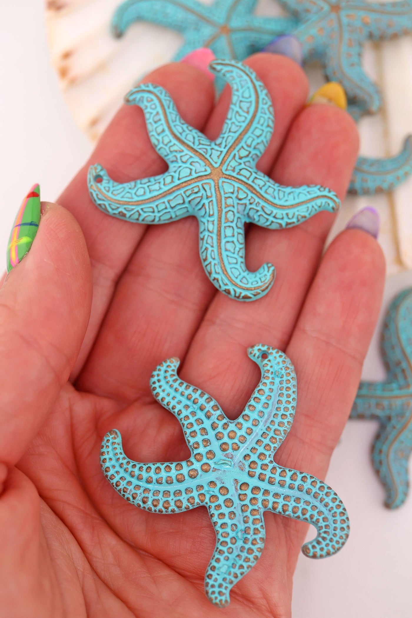 Hand holding turquoise German resin starfish pendant, 48mm, with carved details and brown wash accents.