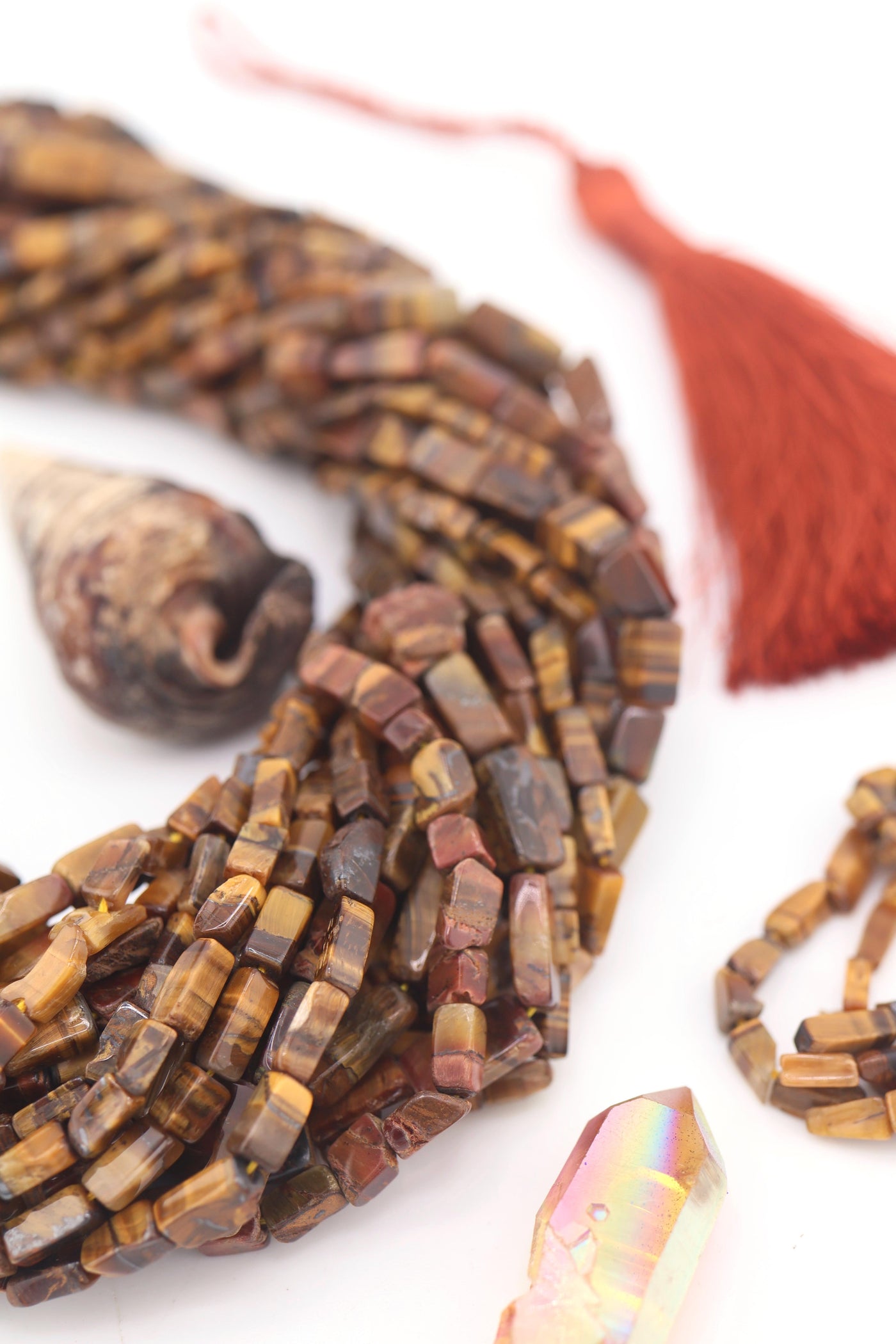 Close-up of natural Tiger’s Eye gemstone beads in rectangular box shape, showing golden-brown shimmer and striped detail, styled with a rust tassel.