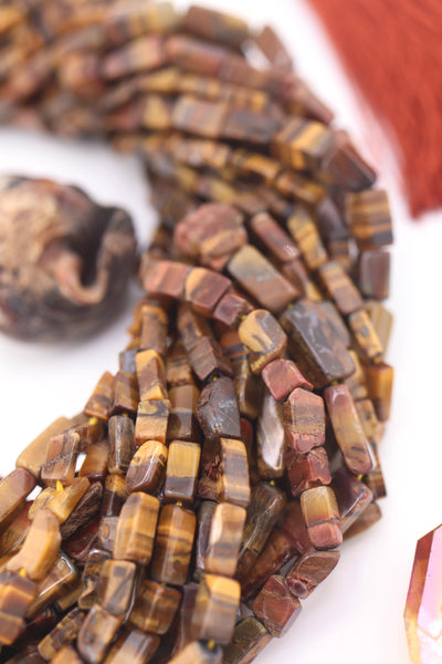 Close-up of natural Tiger’s Eye gemstone beads in rectangular box shape, showing golden-brown shimmer and striped detail, styled with a rust tassel.