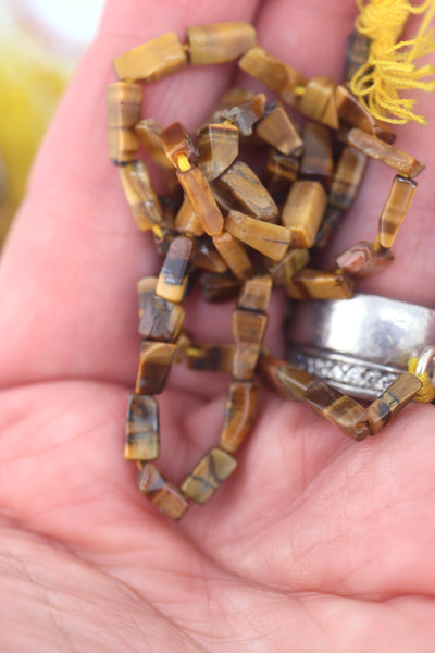 Hand holding a small strand of rectangular Tiger’s Eye beads, showing polished caramel and chocolate tones.