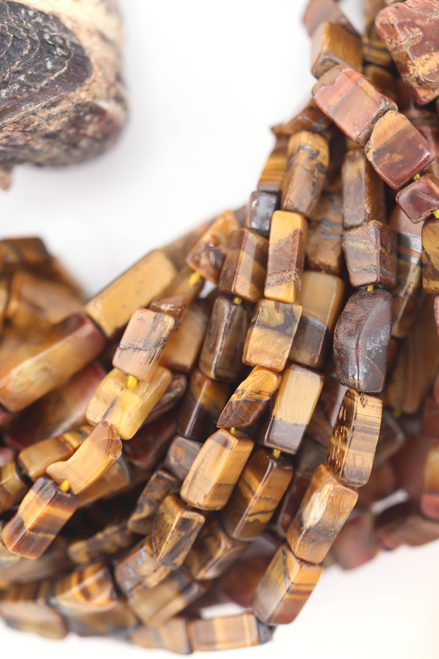 Macro shot of stacked Tiger’s Eye gemstone strands with a glossy, chatoyant surface and earthy color mix.