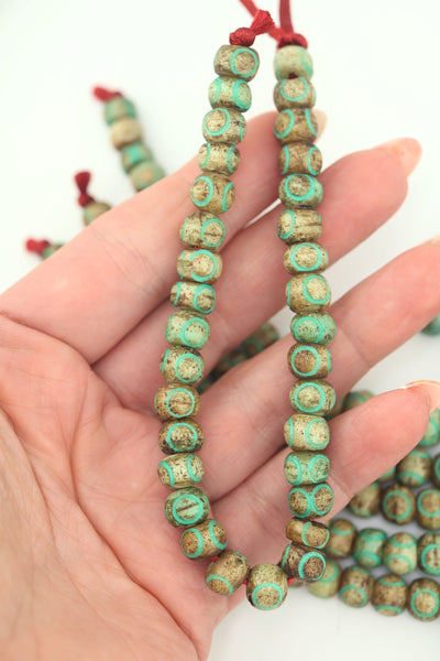 Hand holding strand of 8mm carved bone beads with turquoise carved circles