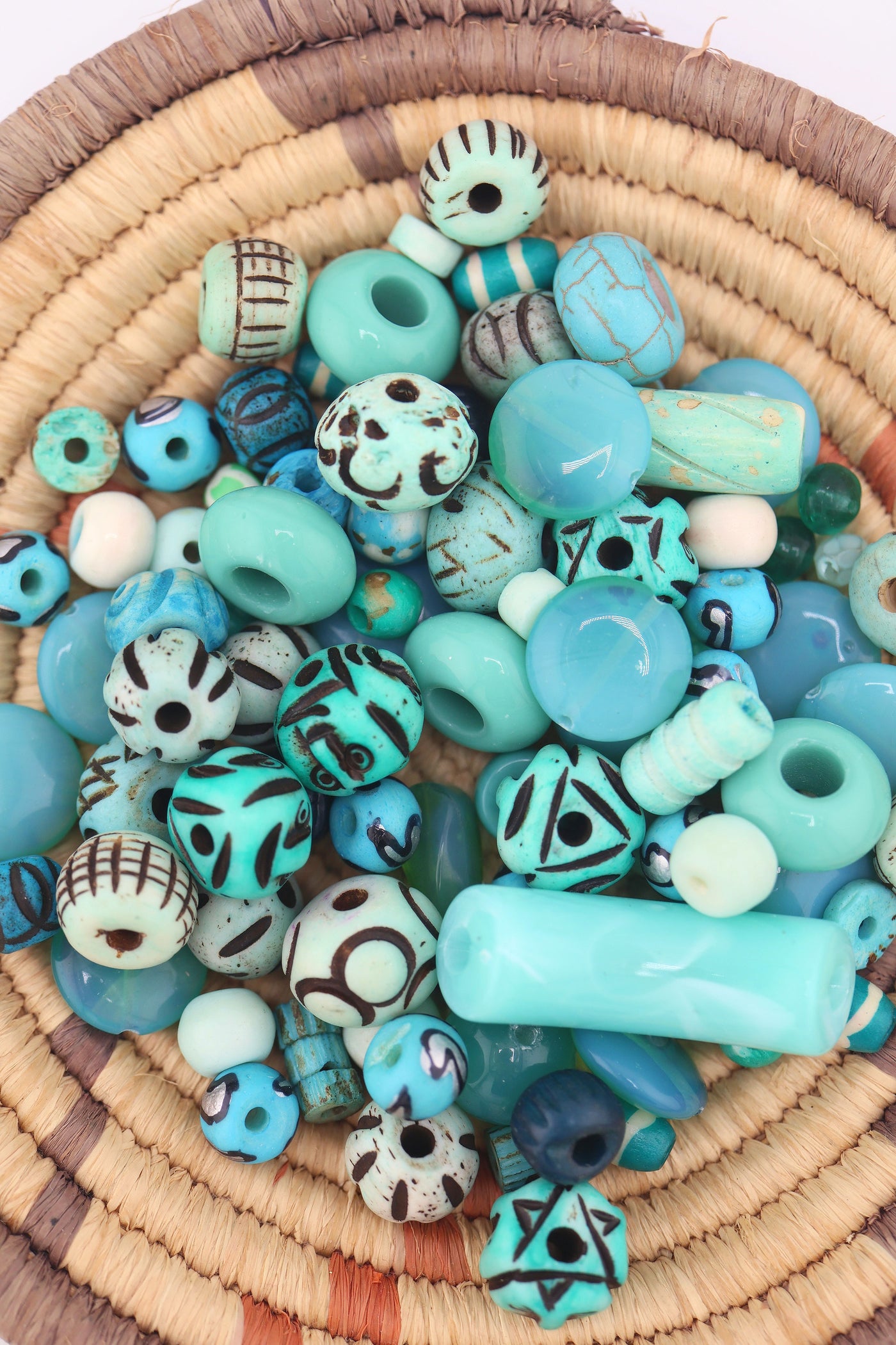Close-up of assorted turquoise beads in a basket, showing round, oval, and carved patterned beads in various finishes.
