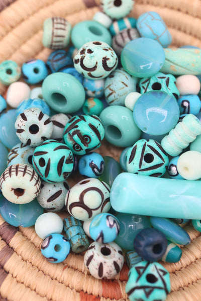 Round woven basket filled with assorted turquoise beads in glass, bone, and acrylic, showcasing carved and patterned designs.