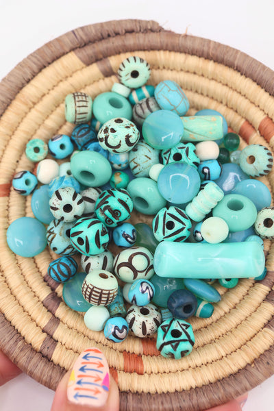 Overhead view of turquoise bead grab bag in a woven basket, featuring mixed shapes, sizes, and carved designs.