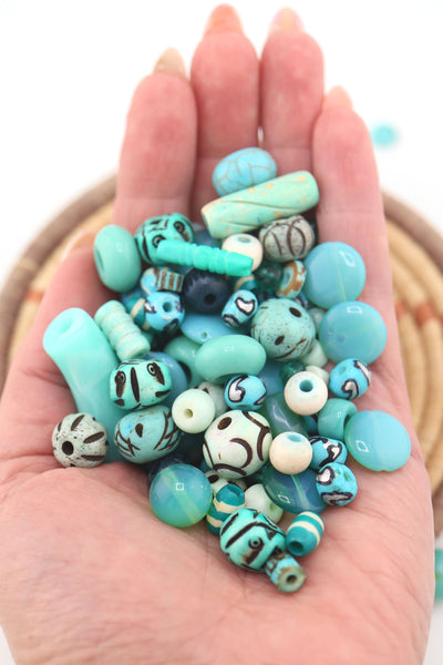 Hand holding a variety of turquoise beads, including round, oval, and carved designs, highlighting textures and patterns.